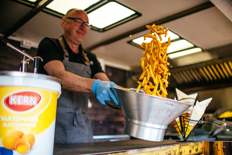 Een medewerker schud de friet door elkaar in een frietwagen