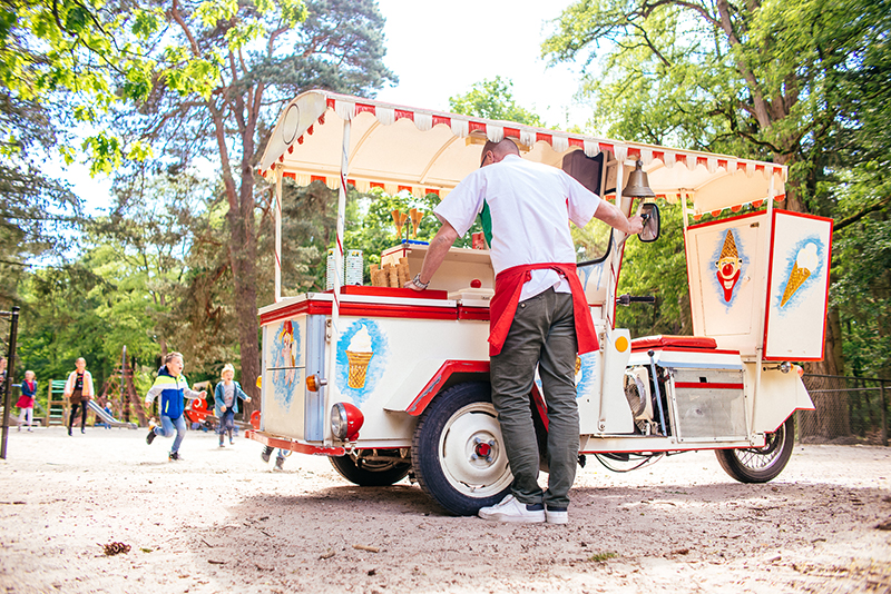 Kinderen in een speelpark rennen op de Pipo ijskar af waar een medewerker klaar staat met een ijsje